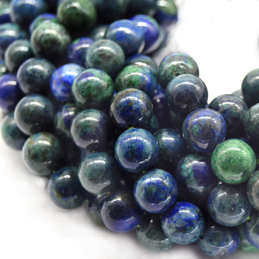Close-up of polished round gemstone beads in deep blue and green with natural speckling, arranged on a white background.