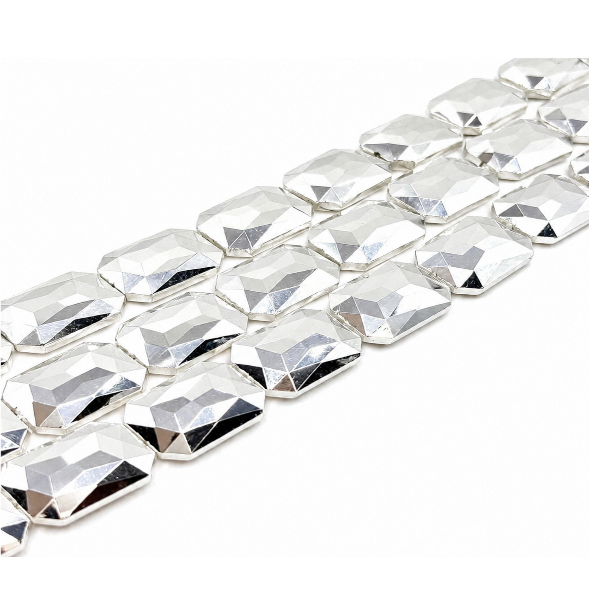  "Close-up of three strands of large shiny silver faceted rectangle crystal glass beads on white background"