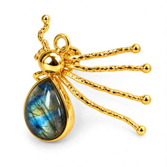 A gold spider-shaped pendant featuring a teardrop-shaped labradorite stone with blue and green shimmer, set against a plain white background.