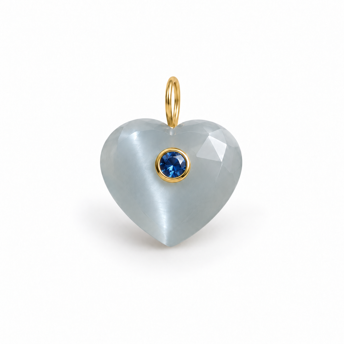 A heart-shaped pendant made of milky white cat's eye with a small bezel-set round blue gemstone and gold-tone ring, shown on a clean white background.
