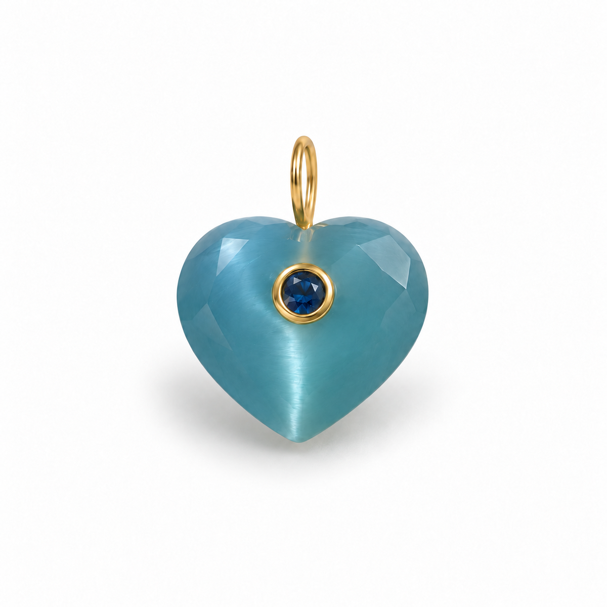 A heart-shaped pendant made of faceted light blue stone with a small round dark blue gemstone in a gold bezel setting and a gold loop at the top, shown on a plain white background.