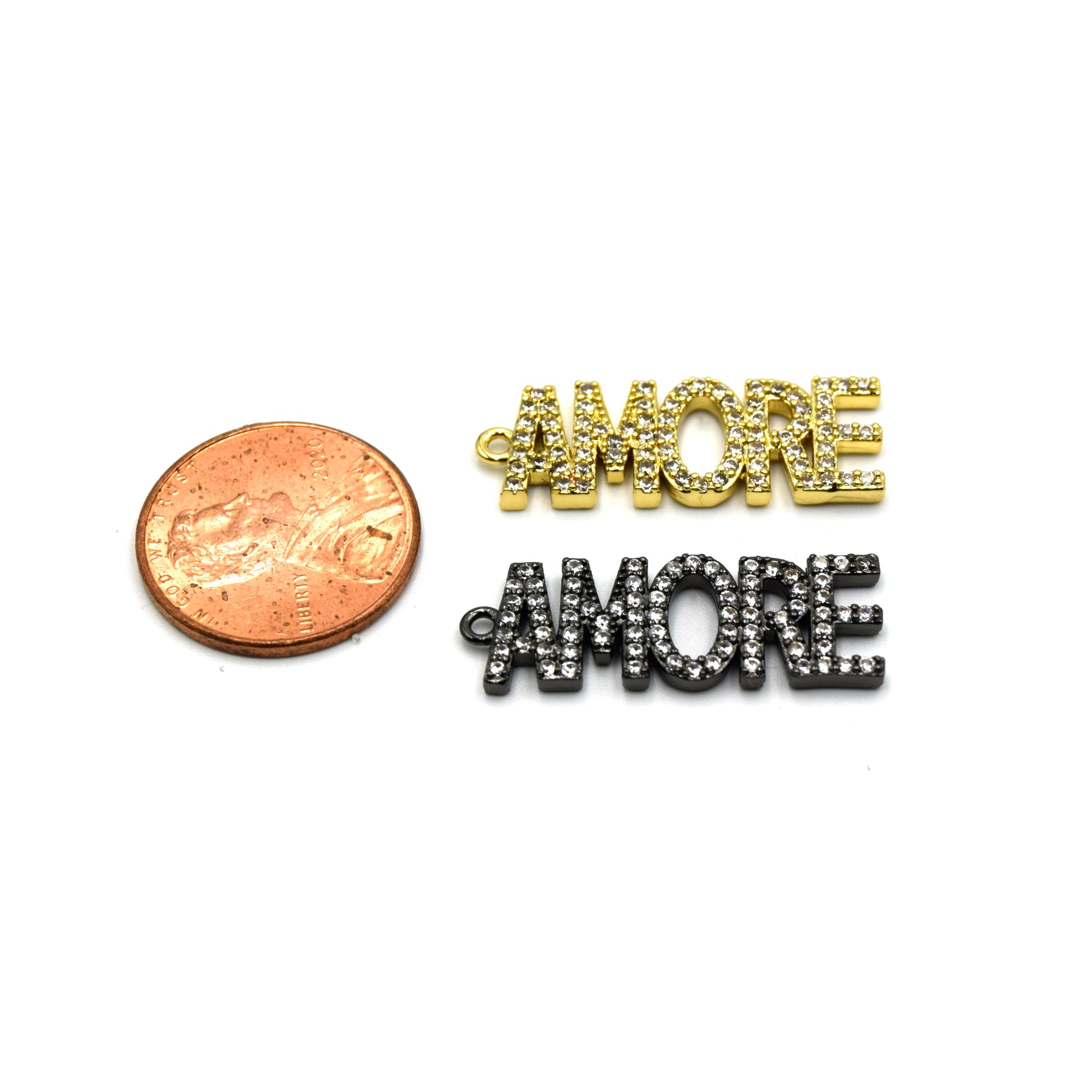 A 14K gold charm shaped into the word "Amore", perfect for expressing your love and affection. The charm is placed next to a penny for sizing reference.