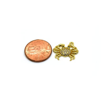 A close-up of a handmade crab pendant for jewelry making, with a penny for size reference. The intricate details of the crab can be seen clearly.