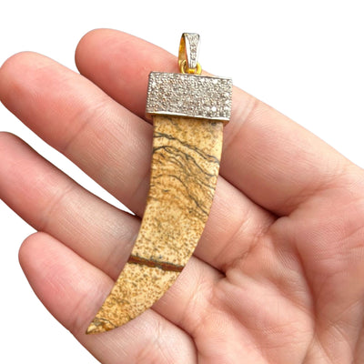 This is a photo of a pave diamond picture jasper pendant. The pendant features a curved jasper stone, with small diamond accents encircling the bail. The pendant hangs from a 14k gold bail.